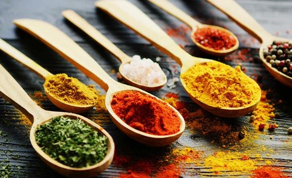 Fundo com diversos condimentos coloridos em colheres de madeira.