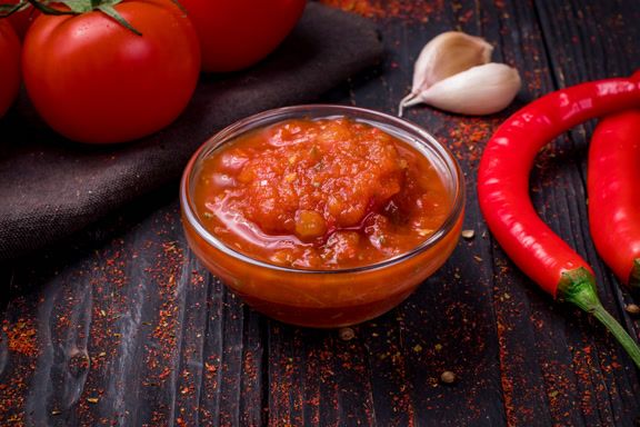 Fundo com uma tigela de molho vermelho e ingredientes frescos.